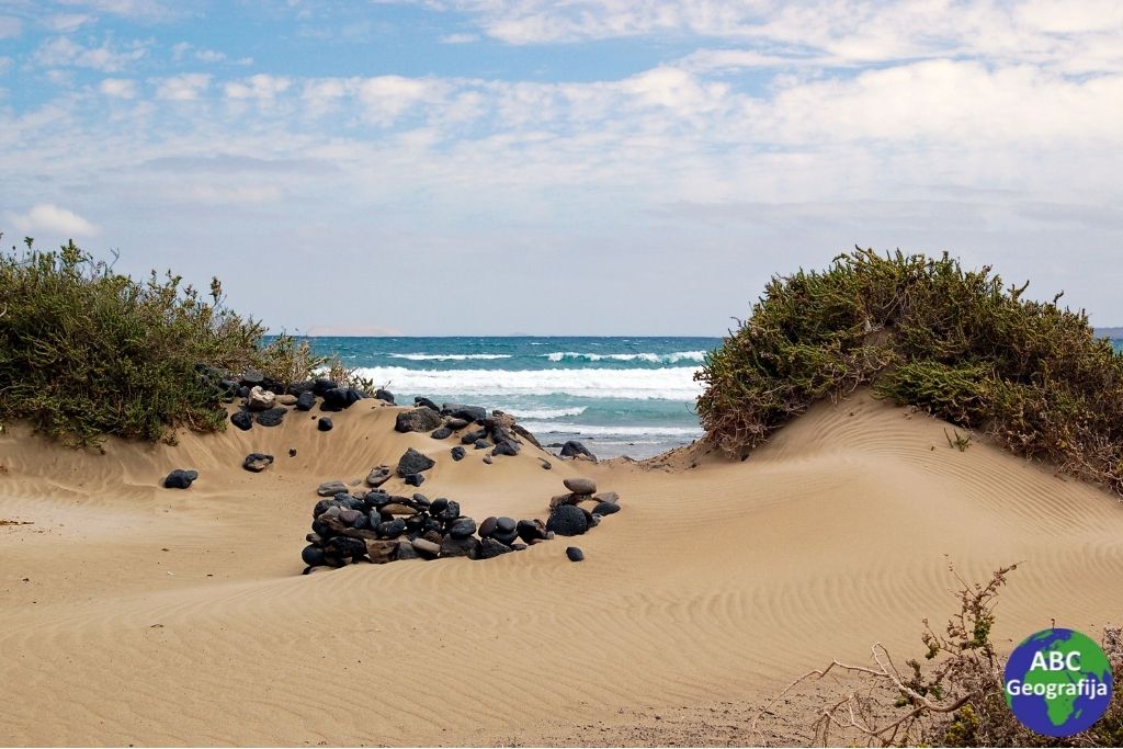 Pješčana plaža na otoku Lanzarote - relativno nove vulkanske stijene prekrivene naslagama akumuliranog saharskog pijeska